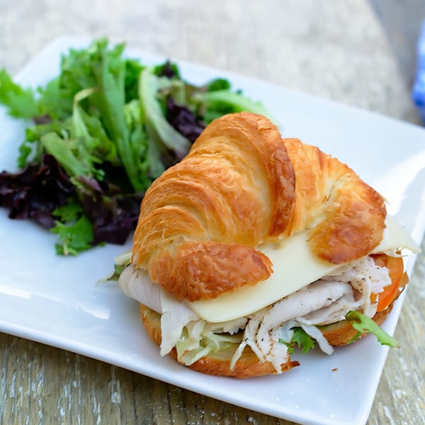 Turkey and cheese croissant sandwich with lettuce and tomato, served with a side salad.