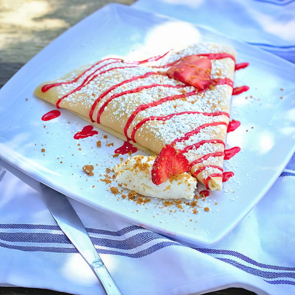 A strawberry crepe from The Crepe Club, drizzled with red sauce and powdered sugar, on a white plate.
