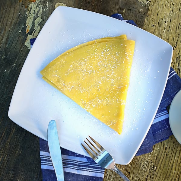 A golden crepe, dusted with powdered sugar, on a white plate with a blue napkin and silverware.