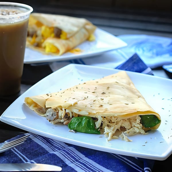 Savory crepe with chicken, mushrooms, and spinach on a white plate with a drink and another crepe.