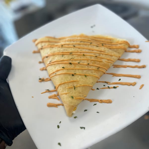 A triangular savory crepe from The Crepe Club, drizzled with orange sauce and herbs on a white plate.