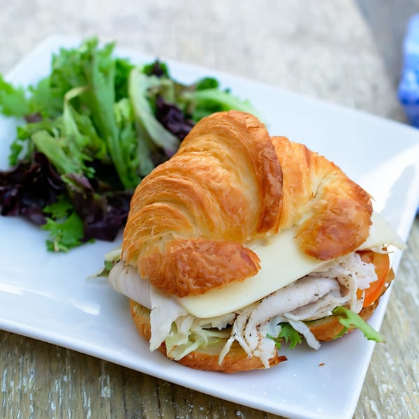 A croissant sandwich with turkey, cheese, and vegetables, served with a side salad.
