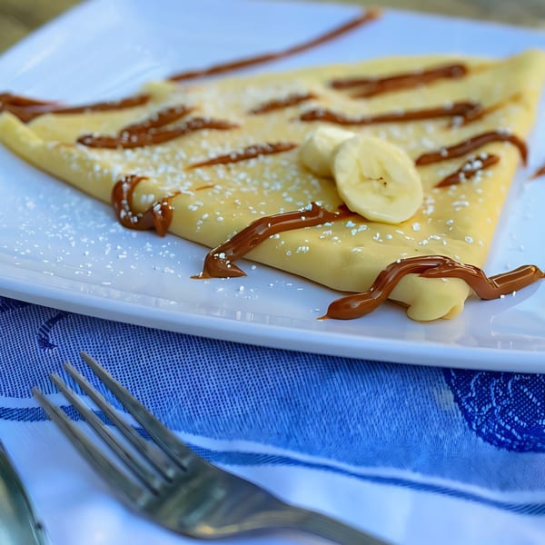 A banana and caramel crepe from The Crepe Club, dusted with powdered sugar on a white plate.